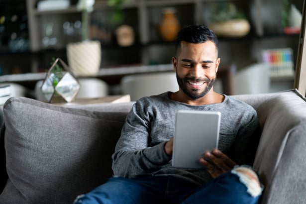 hispanic guy on couch looking at tablet