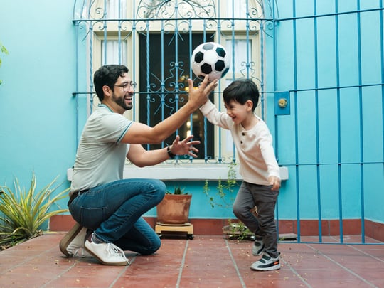 hispanic son and father playing soccer in front of blue house